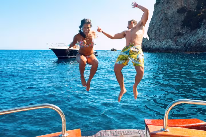 Couple joyfully jumps off a boat into the clear blue waters during Capri boat excursion from Positano.