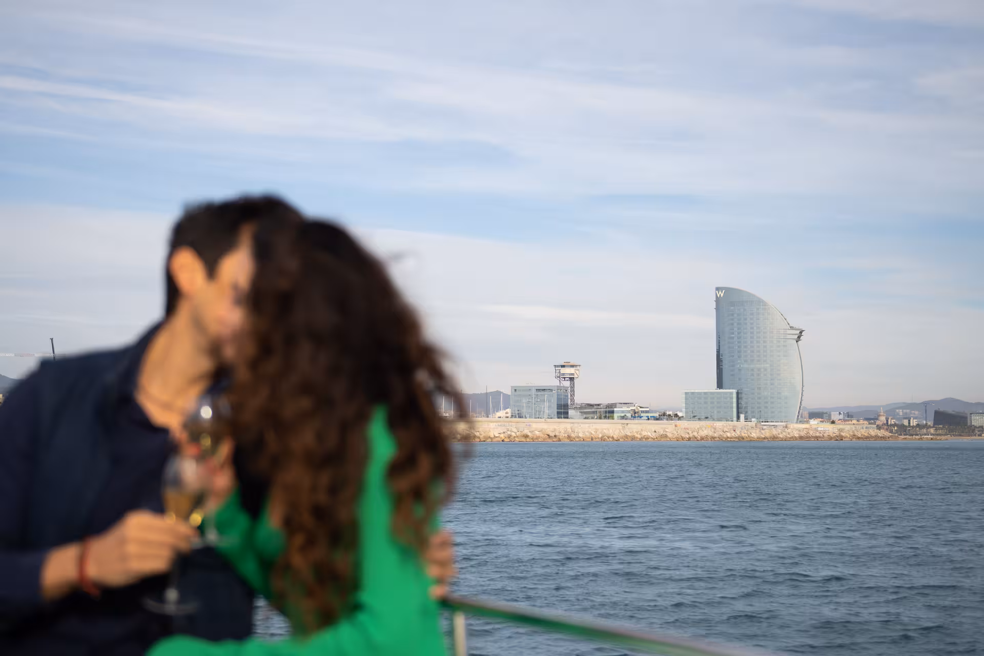 Blurred couple kissing with champagne on a Barcelona yacht, W Hotel skyline backdrop for proposal experience