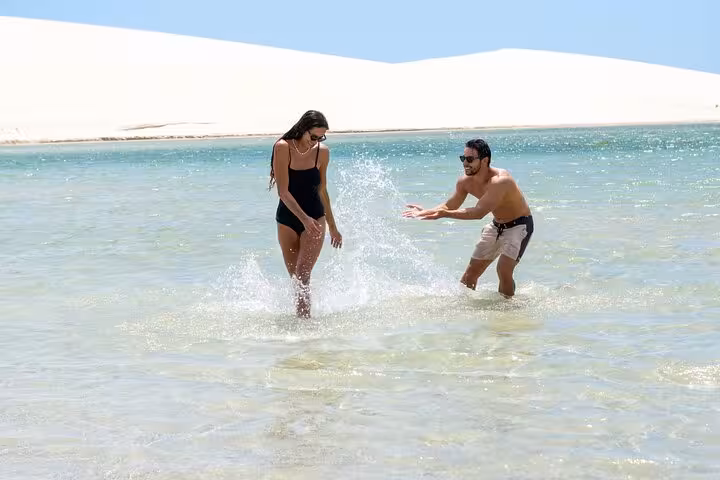 Couple splashing in crystal lagoon by sand dunes, stop on Jericoacoara sunset ATV tour adventure