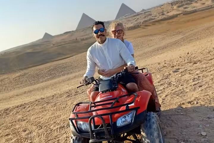 Couple riding red ATV quad in Giza desert with pyramids behind, private pyramids and Sphinx adventure tour