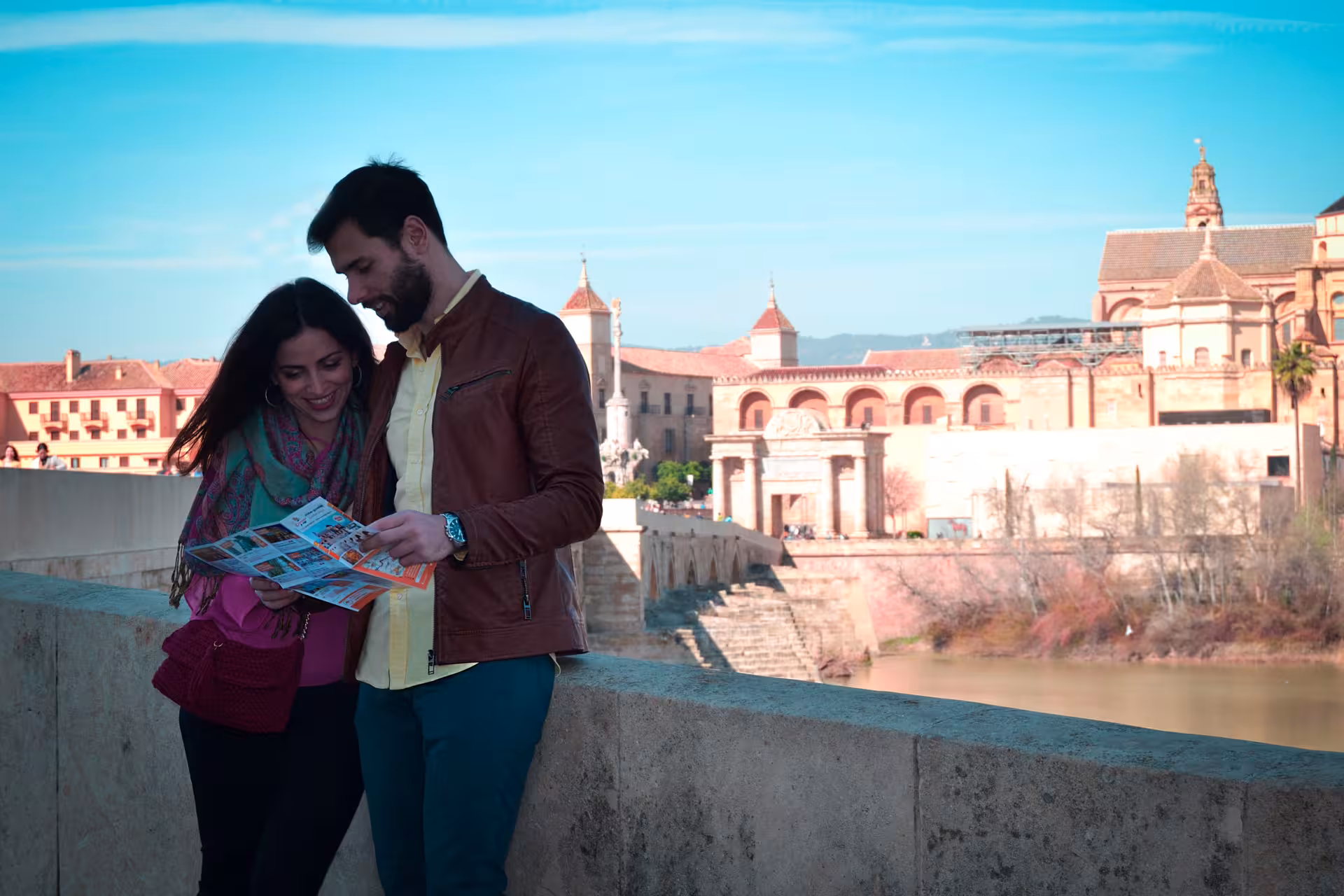 Couple reading map on Roman Bridge with Córdoba Mezquita skyline, perfect for a free walking tour