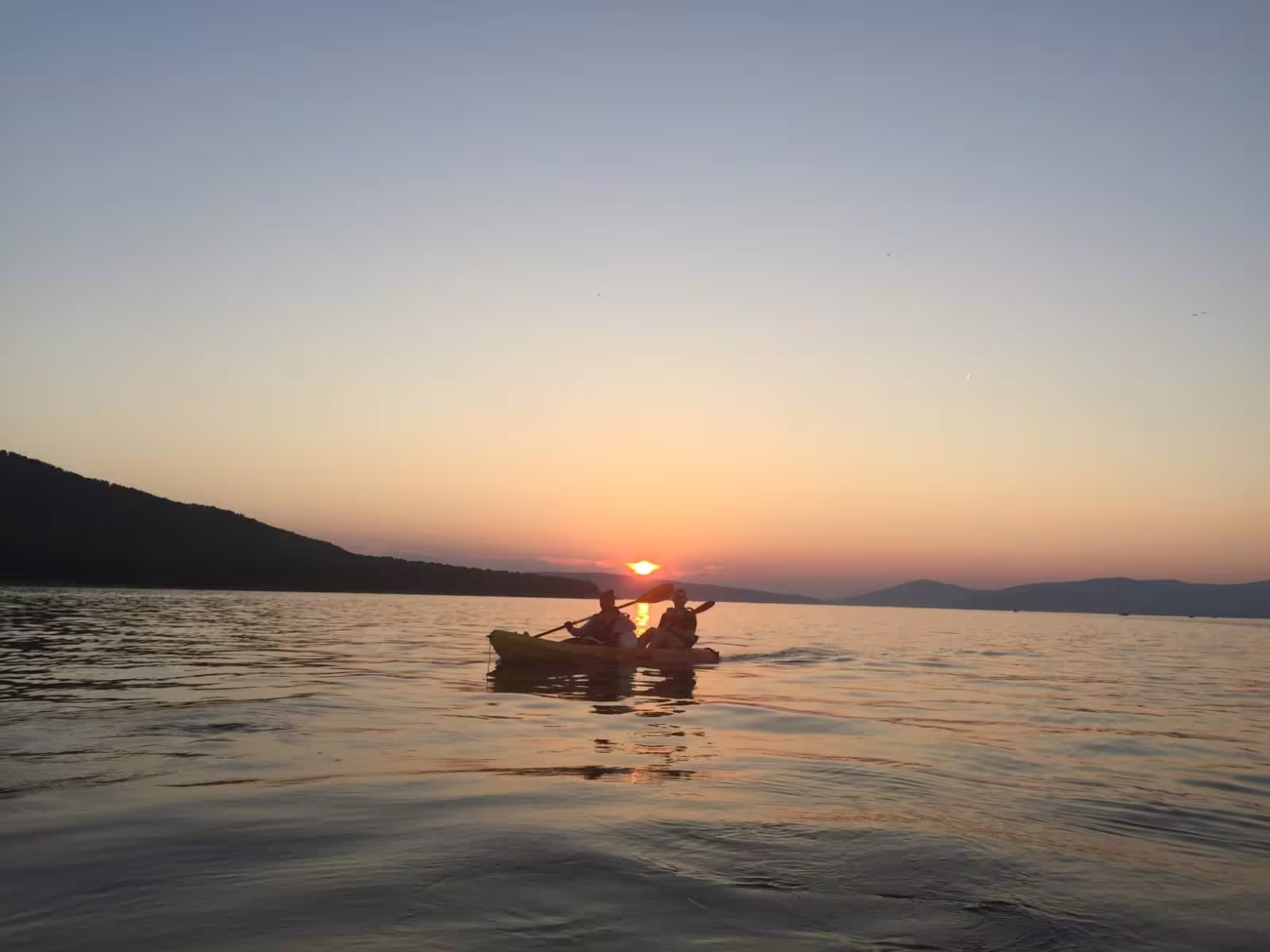 Couple paddling sea kayak at sunset on the Split Riviera, Adriatic Sea, guided evening tour with wine