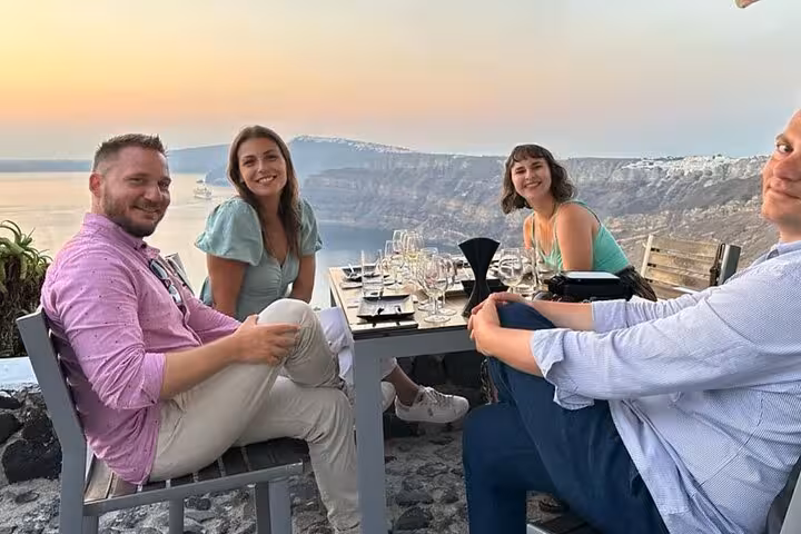 Couple dining at sunset with Santorini caldera views on a customized private tour, Oia cliffs in background