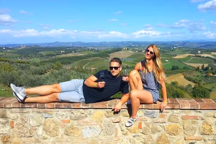 Couple relaxes on a stone wall with panoramic views of Tuscany's rolling hills on a wine tour from Florence.