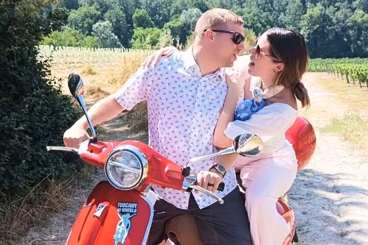 Romantic couple sharing a moment on a Vespa during a Tuscany tour, surrounded by lush vineyards near Florence.