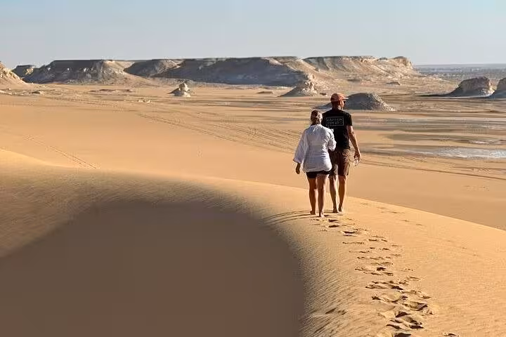 Couple walking along golden dunes in Egypt’s White Desert on a 2-day private White & Black Desert safari tour