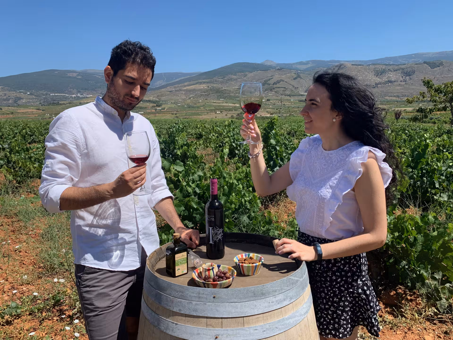 Couple enjoying wine tasting in a scenic vineyard with mountains in the background.