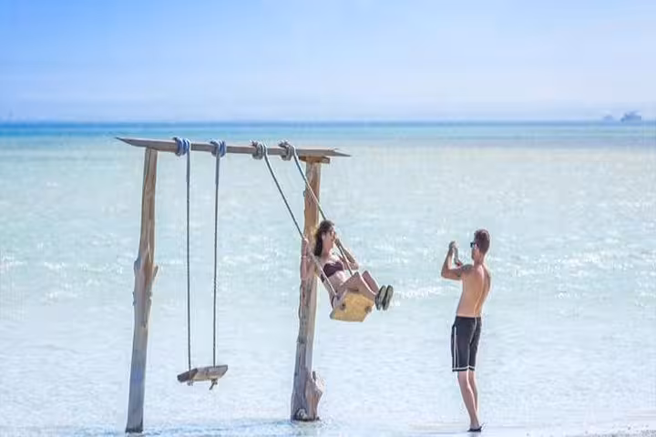 Couple enjoying a wooden sea swing at Orange Bay Hurghada, Red Sea island stop on snorkeling day trip