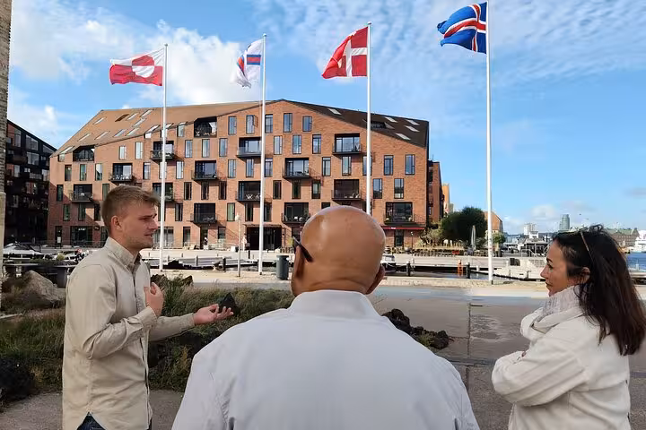 Guide explaining history to tourists near waterfront with flags in the background.