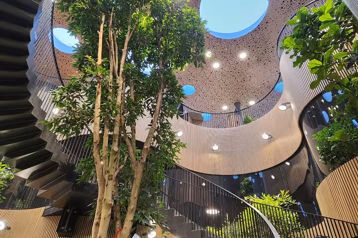 Modern atrium with lush greenery and spiral stairs, showcasing architectural beauty on a cultural walking tour.