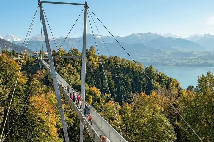 Tourists walking on a picturesque suspension bridge with panoramic views of Swiss mountains and Lake Thun.