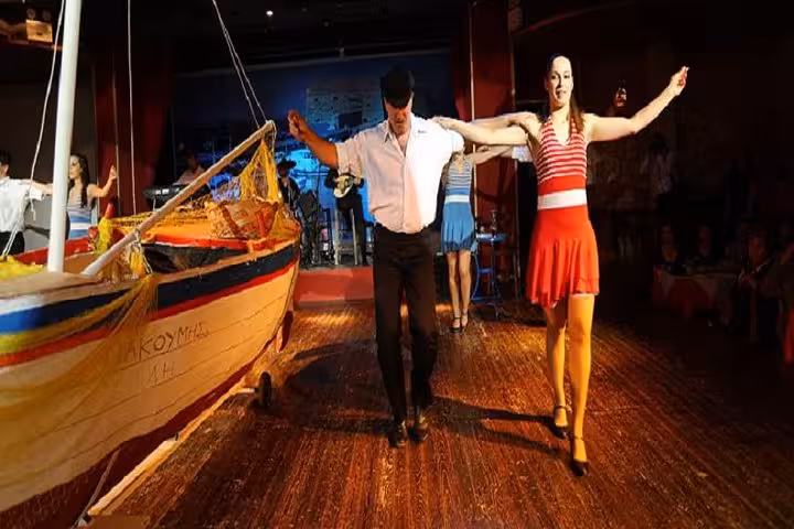 Cretan night show with dancers performing on stage beside a fishing boat set, live music, food and dancing