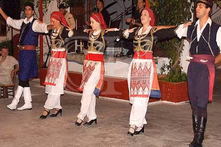 Traditional Cretan dancers in folk costumes performing at a Cretan night with live music, food and dancing