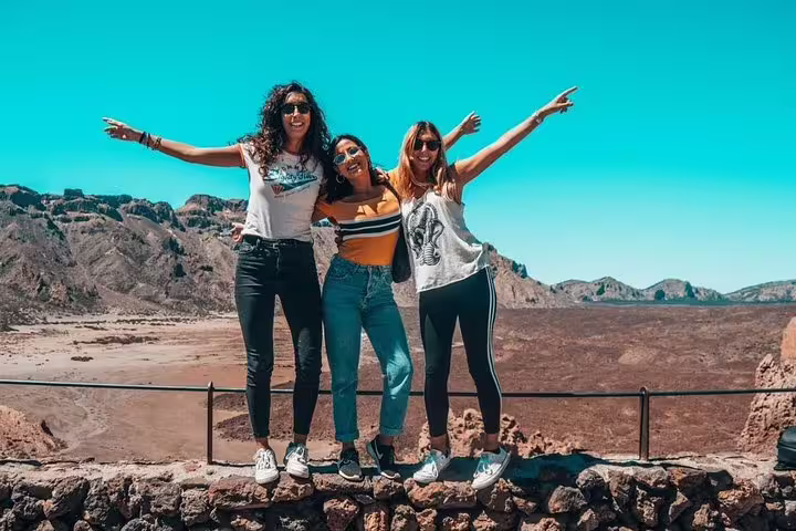 Three women posing happily with arms outstretched against a volcanic landscape, perfect for cruise excursions.