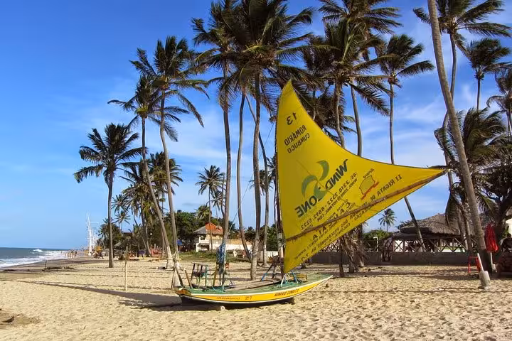 Traditional jangada sailboat on Cumbuco Beach with palm trees, a highlight of the Cumbuco Beach Tour