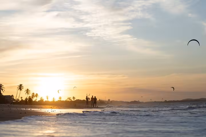 Sunset at Cumbuco Beach with kiteboarding kites, palm-lined shore and waves on a scenic beach tour