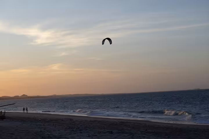Cumbuco Beach Tour view at dusk with rolling Atlantic waves, sandy shoreline and a kite surfer overhead