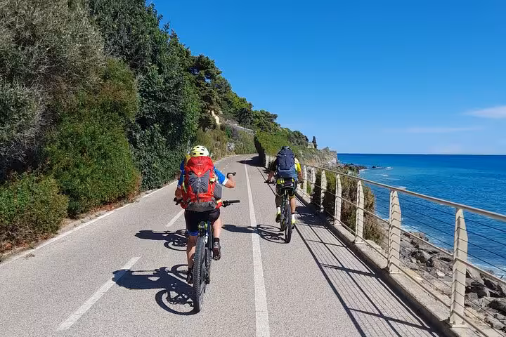 Cyclists ride along the scenic Riviera dei Fiori bike path in Sanremo with stunning coastal views.