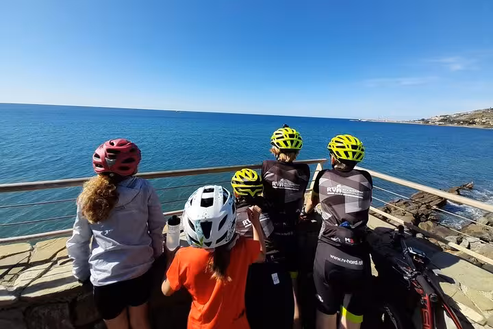 Group of cyclists in helmets enjoy a breathtaking ocean view from the Riviera dei Fiori in Sanremo.
