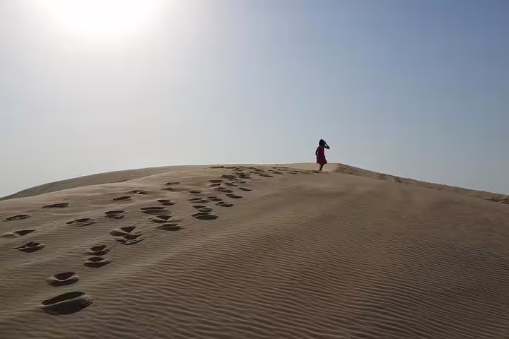 Lone traveler walking across a vast desert dune under a clear blue sky, leaving a trail of footprints in the sand.