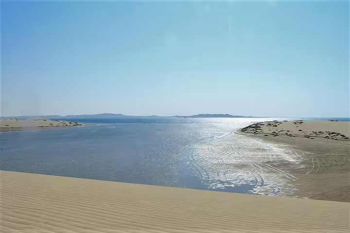 Stunning view of desert dunes meeting a serene body of water under a clear blue sky.