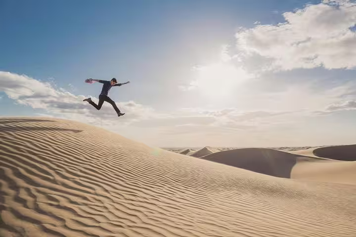 Adventurous person leaping across sunlit sand dunes, capturing the thrill of a desert safari experience.