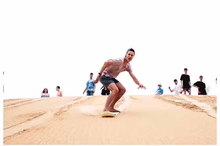 Thrill-seekers sandboarding down a golden dune on the exciting Desert Safari Combo tour.
