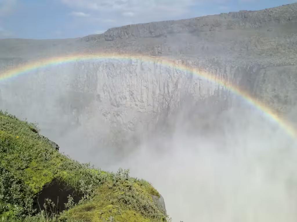 Rainbow over misty Dettifoss waterfall canyon with green cliffs, Diamond Circle Iceland