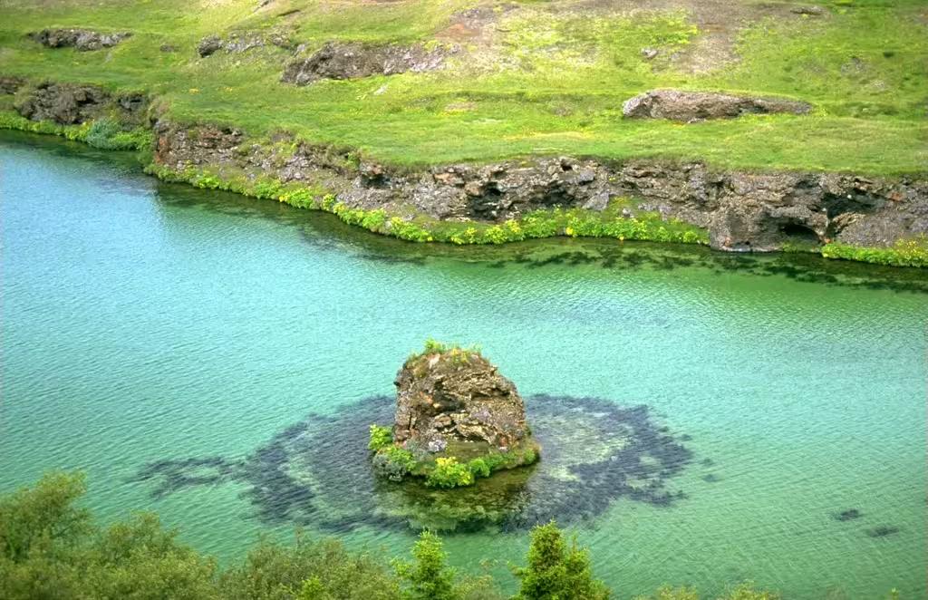 Crystal clear turquoise lake with rocky island and lush green shores near Akureyri, Iceland