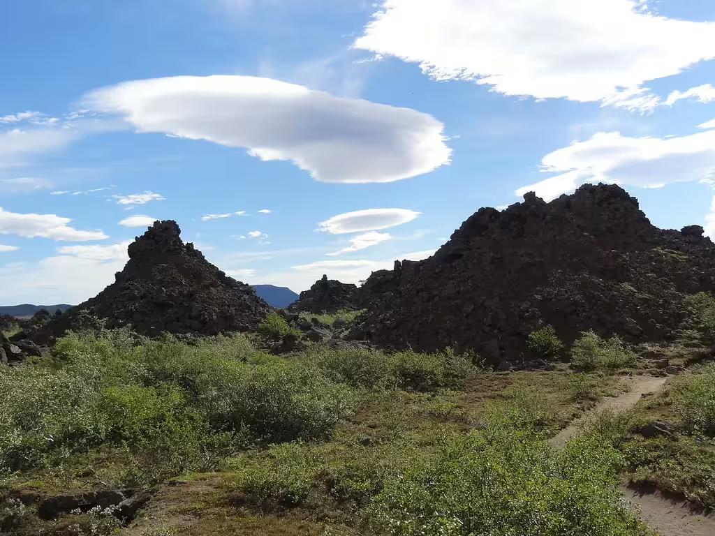 Rugged lava rock formations with green shrubs under blue sky with lenticular clouds, Diamond Circle Iceland