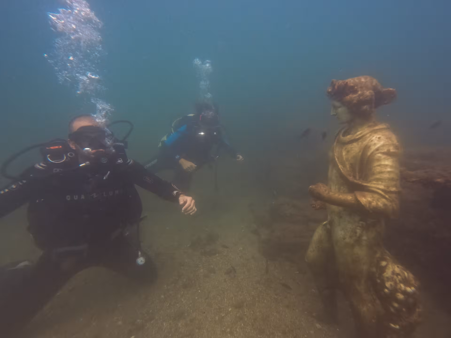Divers posing in front of the statue of the god Dionysus of the "Nymphaeum of Claudius" site.
