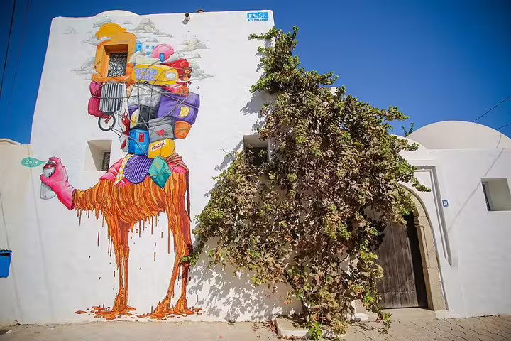 Colorful mural of a camel carrying luggage covers a building wall in the artistic district of Djerbahood.