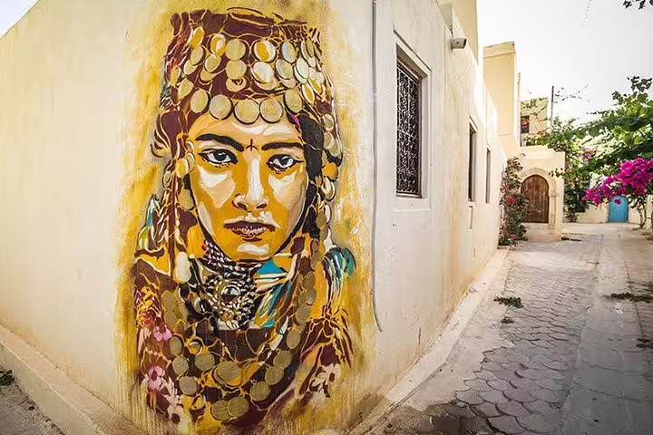 Vibrant street art of a traditional woman adorns a wall in Djerbahood, captured on the E-Scooter Harley Tour.
