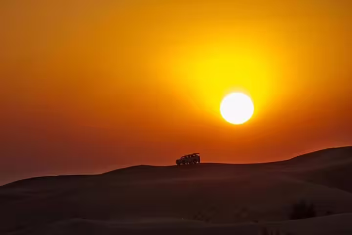 Silhouette of an off-road vehicle against a stunning Doha desert sunset, perfect for dune bashing adventures.