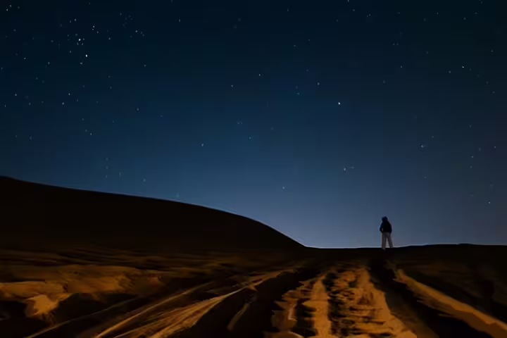 Silhouette of a person atop a dune under a starry sky in Doha, perfect for night desert adventures.