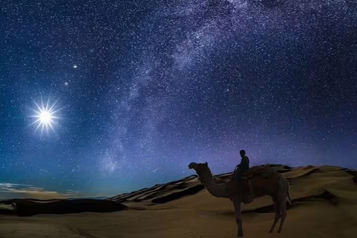 Traveler on a camel silhouetted against a star-filled sky, capturing the magic of Doha night desert safari.