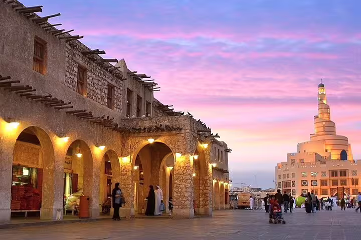 Vibrant sunset over Souq Waqif in Doha, featuring traditional architecture and the iconic spiral mosque in the distance.