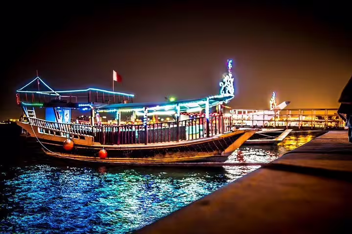 Illuminated traditional dhow boat on Doha's waterfront at night, showcasing vibrant lights and serene waters.