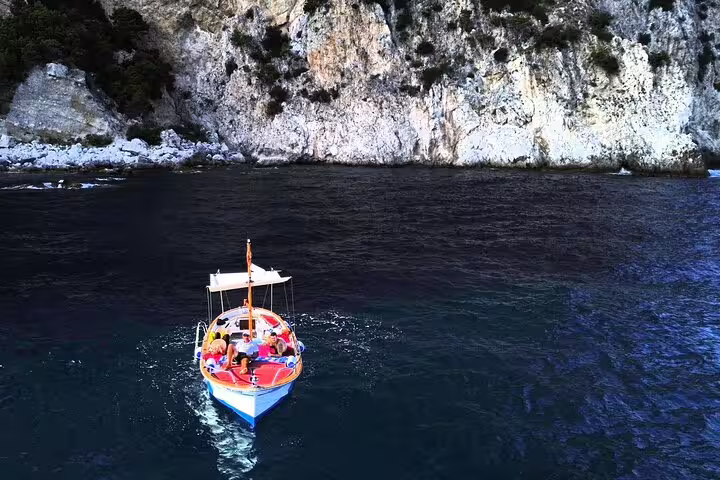 Classic boat cruising Capri coastline by white cliffs on a 4-hour private tour in crystal-clear sea