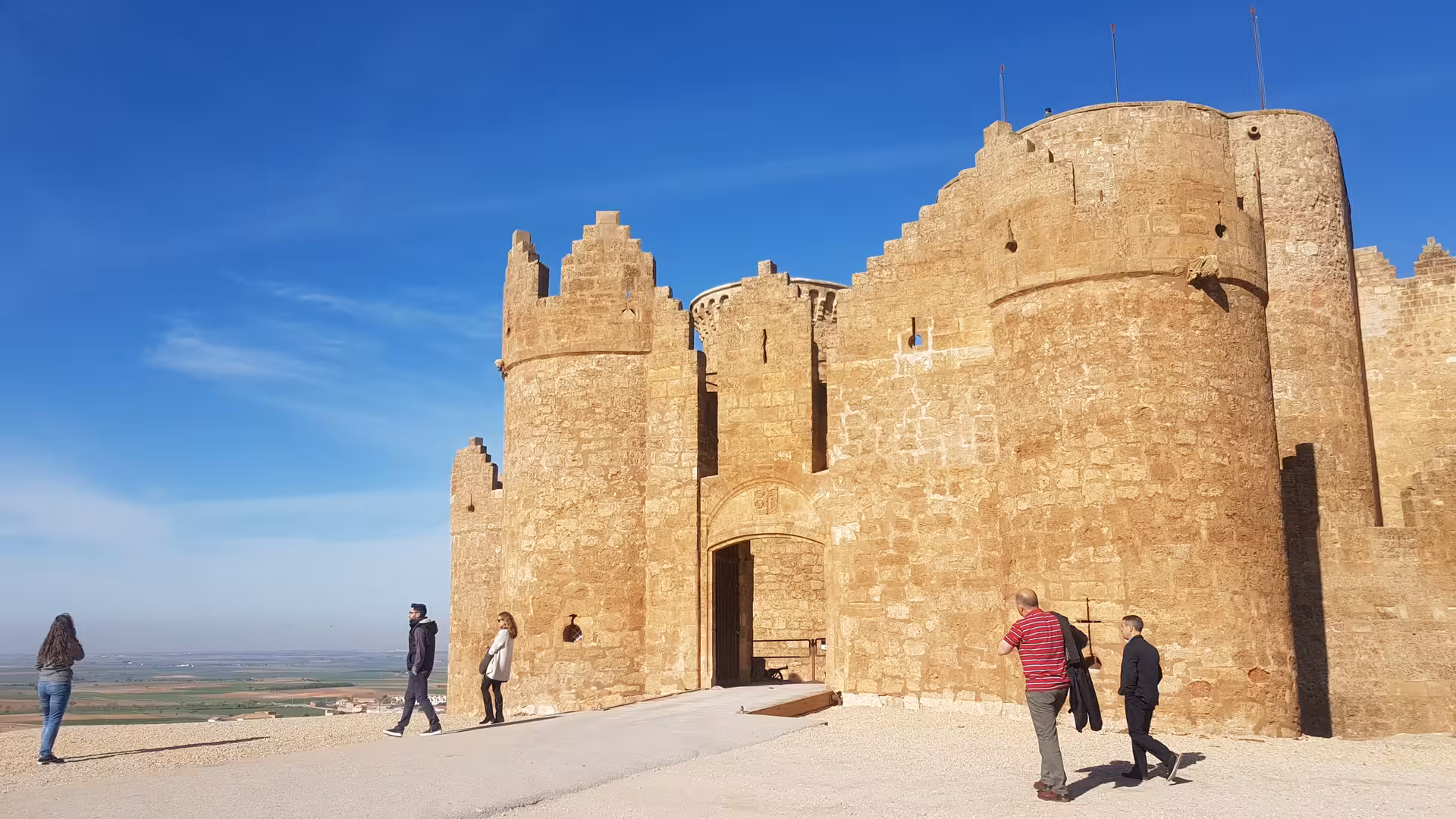 Medieval La Mancha castle viewpoint on a Don Quixote Tour, travelers near the fortress gate under blue sky
