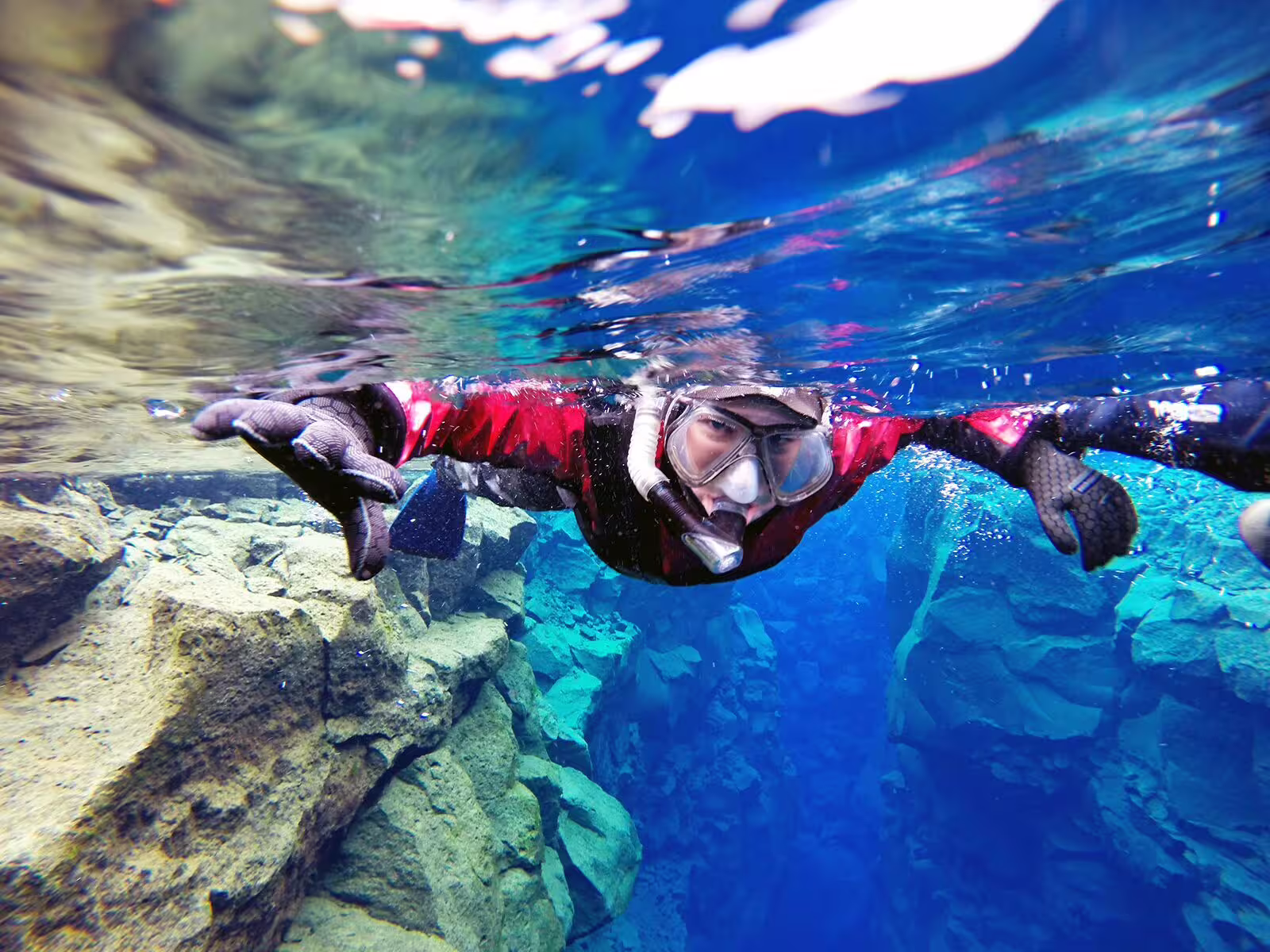 Snorkeler in drysuit explores Silfra's crystal-clear waters between tectonic plates, capturing vibrant underwater photos.
