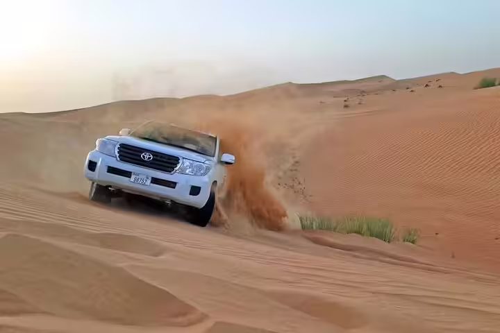 White Toyota 4x4 carving steep dune on thrilling Dubai Desert Safari, kicking up sand at sunset with skilled local guide