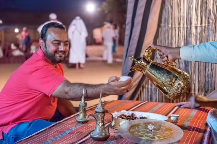 Guest enjoying Arabic coffee and dates served in a Bedouin camp on an evening Dubai desert safari experience