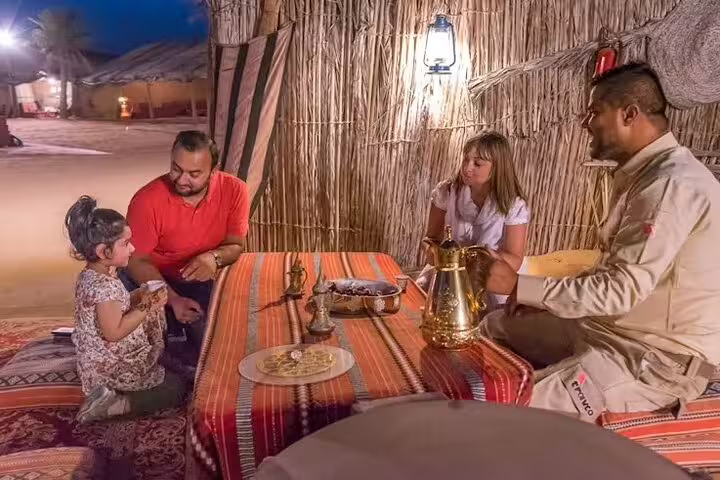 Family relaxing with local guide over Arabic coffee and snacks inside Bedouin tent on Dubai desert safari tour