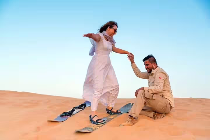 Couple sandboarding on Dubai Desert Safari, local guide helping guest balance on dune before BBQ dinner experience