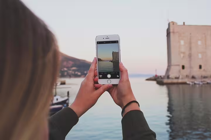 Traveler photographing Dubrovnik Old Town harbor and fort at sunset on a private guided walking tour