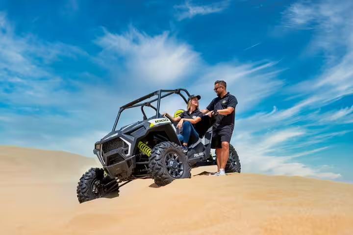 Adventurers enjoy a thrilling dune buggy ride on golden Dubai sand dunes under a vibrant blue sky, perfect for an exciting desert safari.