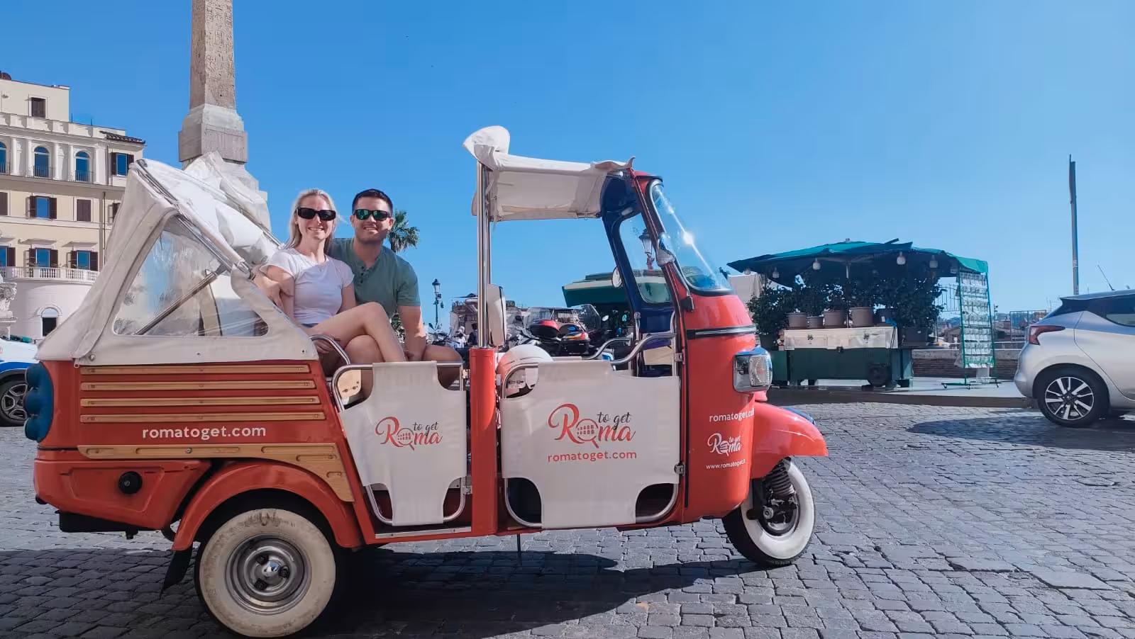 Tourists enjoying an early morning Ape Calessino ride through a vibrant Italian square under a clear blue sky.