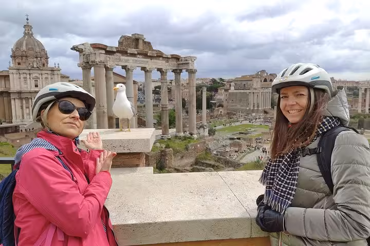 E-bike tourists at Roman Forum with helmets, capturing scenic views and ancient ruins on a cloudy day.