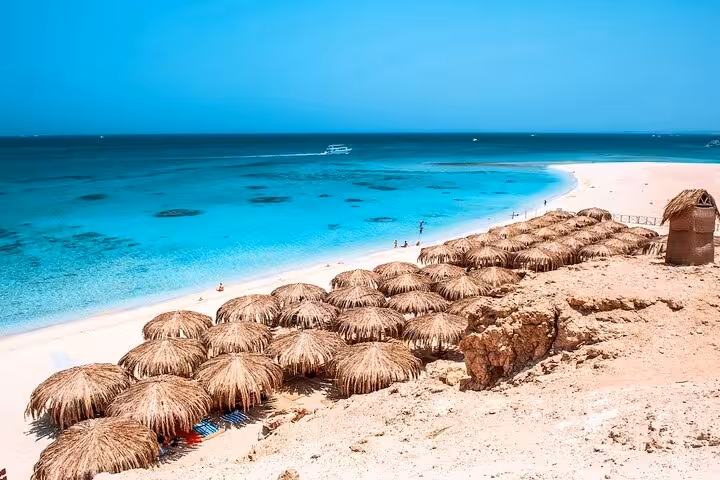 Eden Island sandy beach with straw umbrellas and crystal-clear Red Sea, Hurghada full-day boat trip with lunch